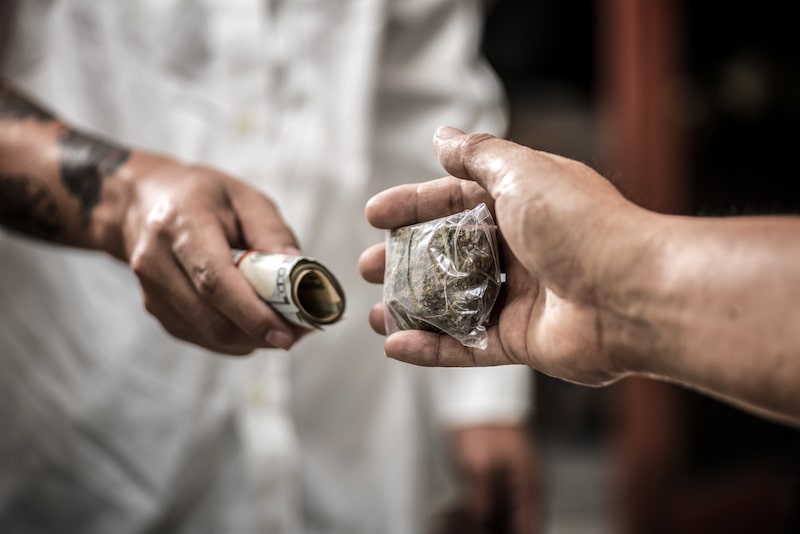 An Exchange Between Two People Where One Is Handing The Other Money And Receiving A Bag Of Green Substance