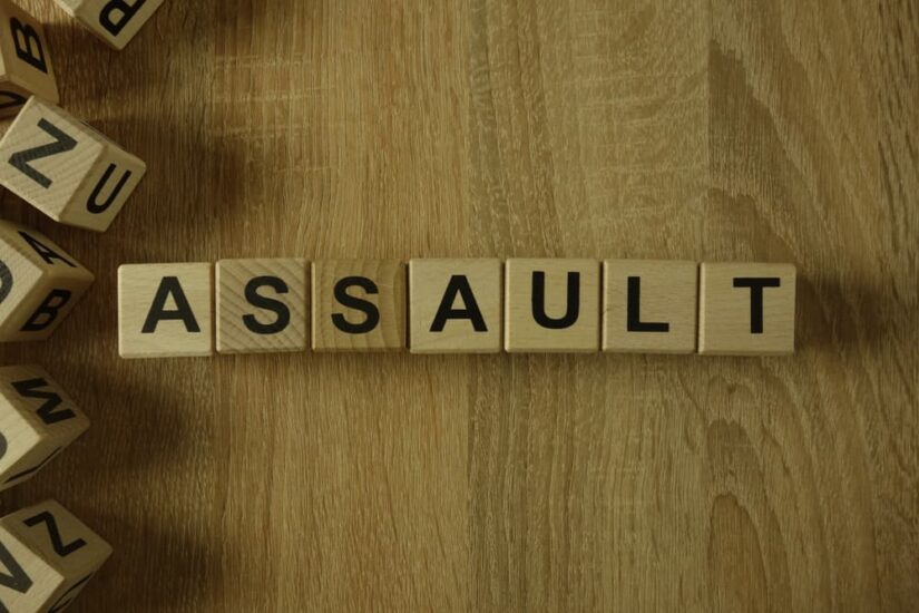 The word 'Assault' formed from wooden blocks arranged on a desk