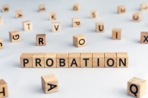 Wooden blocks arranged to spell 'probation', surrounded by random letters. The image represents the concept of probation as a period of time during which a criminal is allowed to stay out of prison or a period to evaluate a new employee's suitability for work.