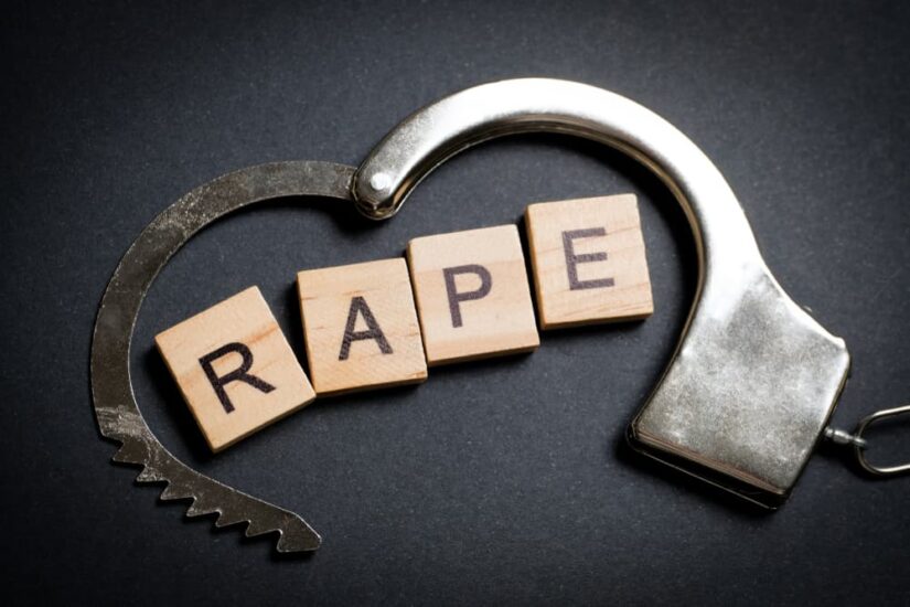 The word made of wooden letters - rape, on a black background in a handcuff.